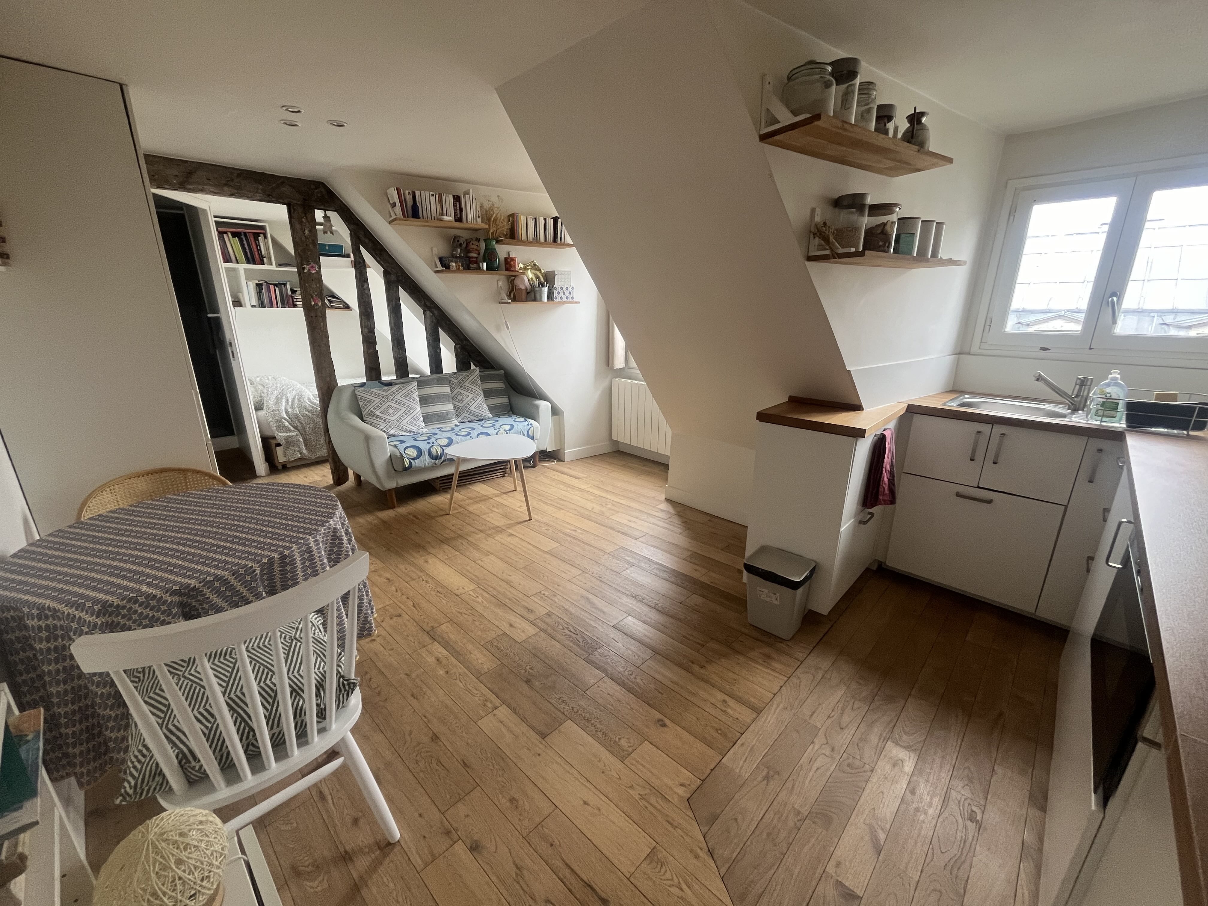 Original photograph of the studio: exposed wooden beams, a sofa, dining table and kitchen beneath the eaves